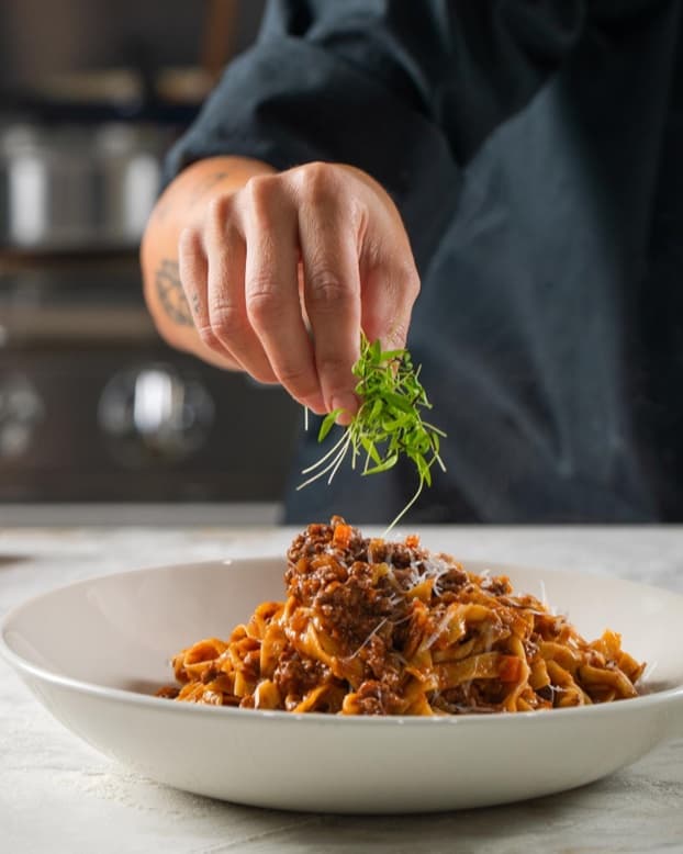 Hands finishing a plate of handmade tagliatelle